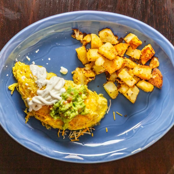 A Rudy's Little Hideaway omelet with guacamole, sour cream, and a side of home fries.