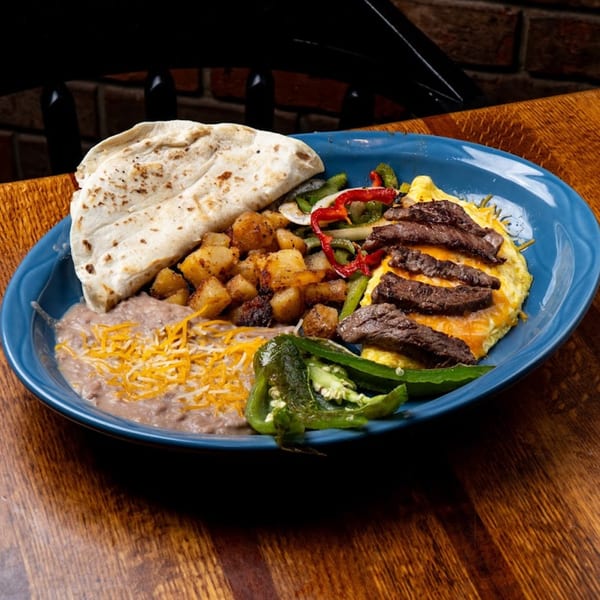 A blue plate with a Mexican breakfast including steak, eggs, potatoes, beans, and a tortilla.