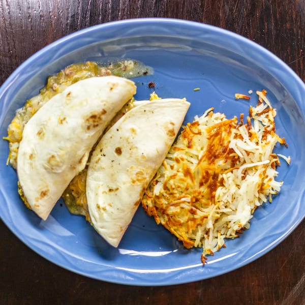 Two Rudy's Little Hideaway enchiladas covered in green chile sauce, served with crispy hash browns.