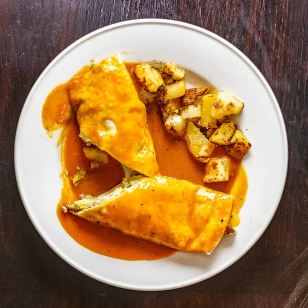 Two enchiladas covered in orange sauce, served with roasted potato cubes on a white plate.