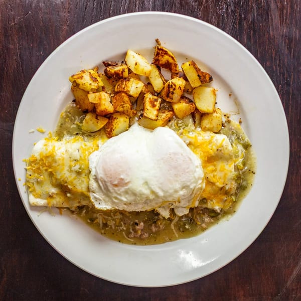 Mexican breakfast plate with enchiladas, green chile sauce, fried eggs, and crispy potatoes.
